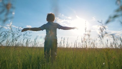 Happy kid in park in field. Kid run his arms to side. Games in park in airplane pilot. Chidhood dream. Kid airplane pilot. Happy kid run in park. Child in field. Child dream at sunset