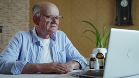 modern medicine, elderly man communicates with doctor online via video communication using laptop while sitting at home at table during quarantine isolation