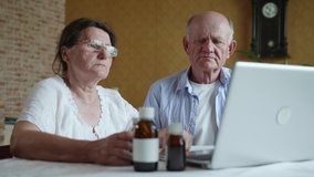 telemedicine, elderly man and old woman in glasses for vision consult doctor about medicines and tablets on webcam sitting at table with laptop in room