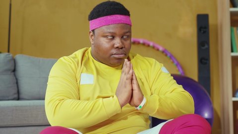 Happy slim young man wearing sportswear and taking smartphone videos of his funny coach. Calm african young man meditating in relaxing lotus pose. Sports fun concept.