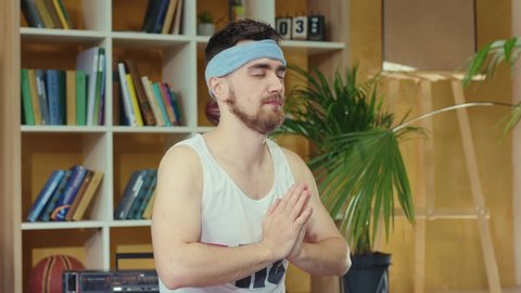 Cunning young bearded man practicing yoga exercise, meditating on fitness mat and spying his trainer repeating moves. Concept of sport, activity, and fun.
