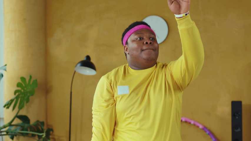 Sportive fat afro-american young man engaged in fitness training at home. Excited retro style black guy dancing and doing aerobics session workout. Sportive humor, fun concept.