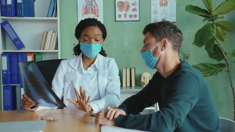 Young female doctor checking x-ray lungs, consulting a patient positive for coronavirus supporting. Caucasian man is frustrated of receiving bad news diagnosis. Medical concept.