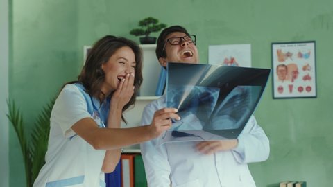 Crazy doctor and nurse practitioner making fun of patient diagnosis looking at lungs x-ray laughing very hard. Concept of humor, medical mistake.