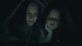 Night insomnia. Family late movie. Two sisters watching video on phone discussing under blanket.