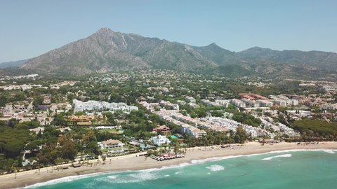 Cinematic aerial view of exclusive area in Marbella, Casablanca beach, golden mile. La Concha mountain in background. Most expensive area from south of Spain, Costa del sol. Drone going backward.