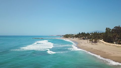 Golden mile Nagueles Beach situated in Marbella exclusive and expensive area south of Sapin Costa del Sol Malaga Province. Sunny day , Green water colour palm tree waves. Nobody. Drone backwards
