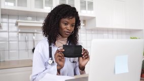 A black female doctor teaches at home using a video call application on her computer to show how to wear a medical mask. The concept of quarantine education.