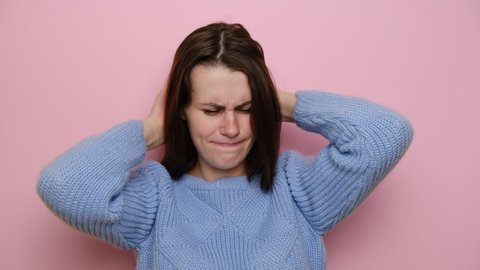 Unhappy young woman isolated on pink studio background. scratches head with hands caused by lice parasites invasion or dandruff, pediculosis and seborrhea, feels discomfort, dressed in blue sweater