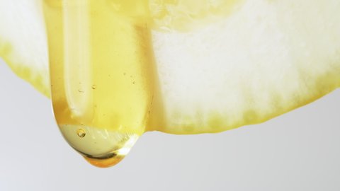 Macro Texture shot of Honey dripping down a fresh lemon slice on white. Freshness, citrus and flu remedy concepts. Slow motion Red Camera.