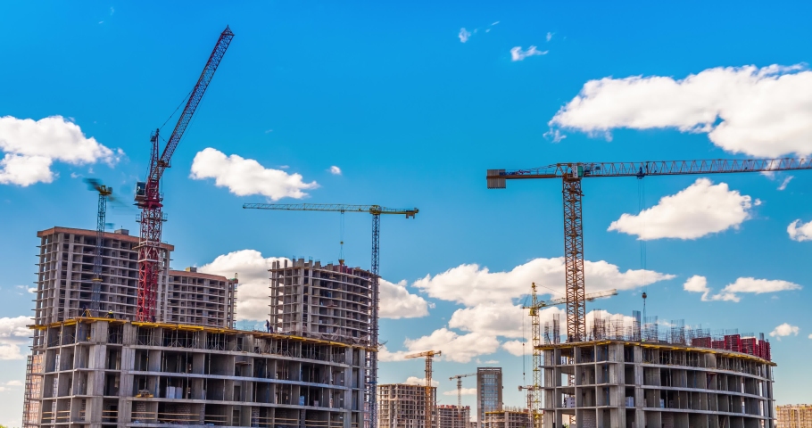 Large construction site with busy cranes. Tower cranes working on a construction site lifts a load at high-rise building. Summer blue sky. Time-lapse.  Royalty-Free Stock Footage #1054486163