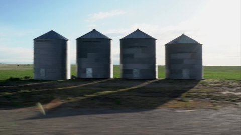 A drive by along recently planted fields  with large metal grain silos on the Canadian prairies in Alberta Canada highlighting the agriculture industry.