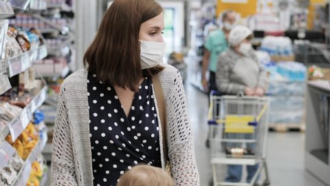 Woman in protective surgical mask walks through supermarket. Medium shot