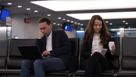 Woman stare to phone, man using laptop, two people sit at airport lounge wait for boarding time. Colleagues wear formal smart casual clothes, portrait shot of two