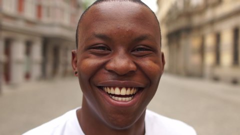 Portrait of black man very happy, smiling in urban background. An african american student sincerely smiles while standing in the middle of a city street. The guy is wearing a white t-shirt