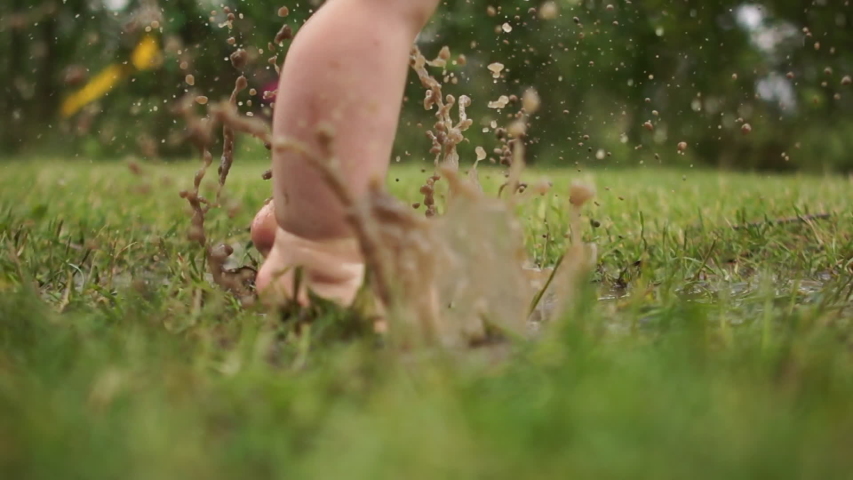 A kid having loads of fun jumping in mud puddle. Clouse up portrait of toddlers bare feet, a child jumping in the grass through a puddle, a happy childhood, have fun