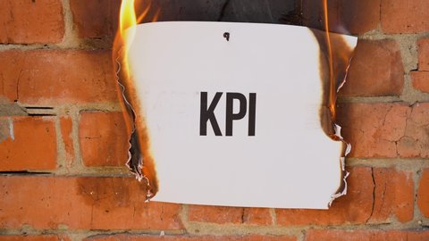 The inscription on a white A4 size sheet against the background of an orange brick wall. The paper with the black KPI burns, smoke and turns into ashes. Business concept.