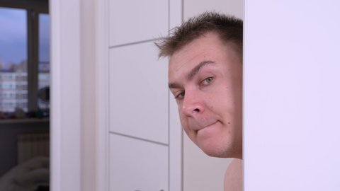 Young disheveled man peeks out from the white room door and quiet goes to somewhere. Undressed male suspiciously sneaks from the bathroom. Indoors. 