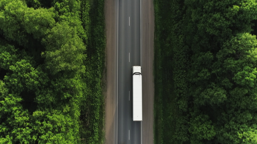 One Semi Truck with white trailer and cab driving / traveling alone on dense flat forest asphalt straight road, highway top down view follow vehicle aerial footage / Freeway trucks traffic Royalty-Free Stock Footage #1054507820