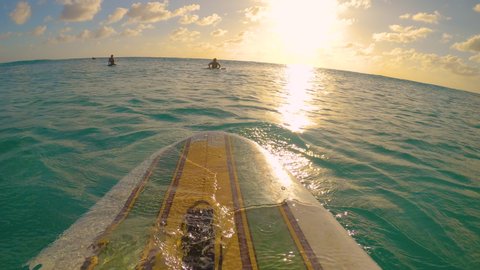 POV, LENS FLARE: Sitting in line up on a vintage longboard, observing the golden sunset during a fun surfing trip in the Caribbean. Surfer sits on surfboard and waits for waves on a sunny evening.