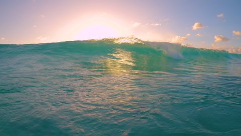 SLOW MOTION, CLOSE UP: Small tube wave sweeps over the camera on a sunny summer evening in the Caribbean. Idyllic shot of a turquoise barrel wave rolling over the camera filming the golden sunset.
