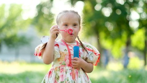A girl with Down syndrome blows bubbles. The daily life of a child with disabilities. Chromosomal genetic disorder in a child.