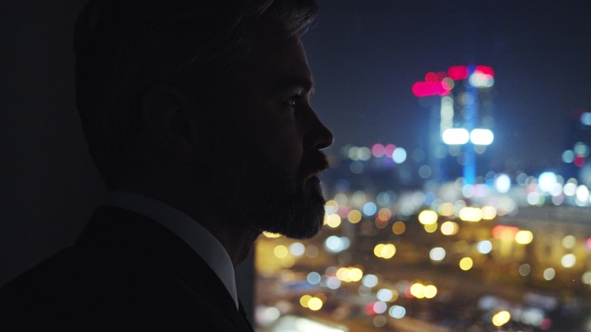 Close-up successful bearded businessman boss alone with his thoughts standing at window looking forward into future. Spectacular night cityscape. Warsaw, Poland. Royalty-Free Stock Footage #1054512893