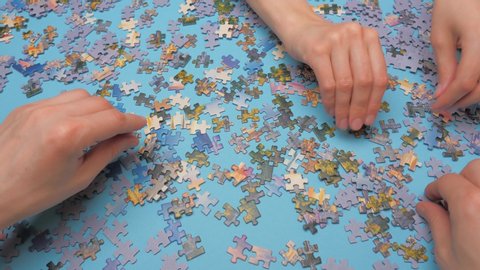 Placing pieces of puzzle face up. Family leisure time. Four hands assembling puzzle. Oddly shaped interlocking and mosaiced pieces of jigsaw. Fully interlocking puzzle. Jigsaw puzzle enthusiasts