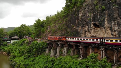 Aerial view, travel train of Death Railway "Krasae cave" line beside the cliff, Amazing Train on The Bridge of the River Kwai at Kanchanaburi amazing Thailand. Aerial view slide and pan.