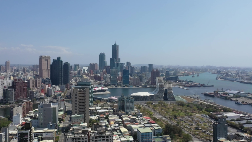 Aerial skyline of Kaohsiung, a vibrant seaport city in Southern Taiwan, with 85 Sky Tower among skyscrapers by the harbor & the futuristic architecture of Music Center by the Love River under blue sky