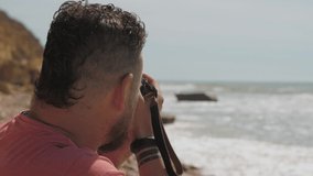 close-up. A bearded man holds a camera in his hands and takes pictures of sea landscapes. back view .professional photographer. slow motions. 