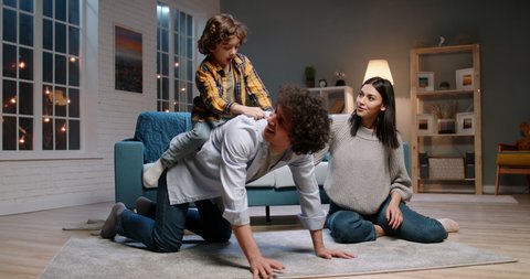 Funny asian family relaxing at home together. Little kid with curly hair jumping onto his father, doing a piggy back ride and laughing - happy family, recreational pursuit 4k footage