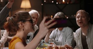 Happy large caucasian family celebrating christmas together at dinner party table, having video chat on smartphone with distant relatives or friends, smiling - holiday, communnication 4k footage