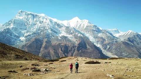 Couple trekking to Ice lake, part of the Annapurna Circuit Trek, Himalayas, Nepal. They are happy. Annapurna chain in the back, covered with snow. Clear weather, dry grass, snowy peaks. High altitude
