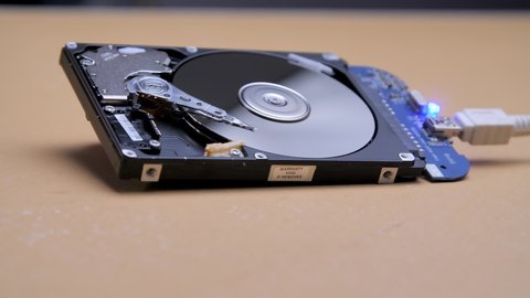 Work of hacked open hard drive inside. Hacker breaks sensitive data from a hard drive. Repair hard disk drive with spinning platter. Close-up of magnetic head. Internal Structure of HDD lies on table.
