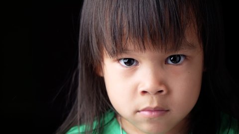 Portrait face of Asian little child girl with angry expression on dark background.