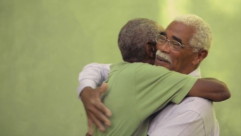 Retired old men and lifestyle, happy senior black brothers talking and hugging outdoors. Elderly African american friends embracing, smiling, speaking. Emotional reunion of veterans
