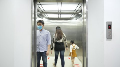Asian people wearing protective hygienic mask walking get in elevator and standing in corner of elevator for social distancing to avoid coronavirus. New Normal, Virus protection concept. 