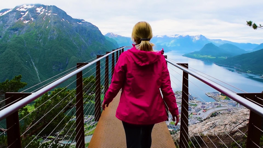 Hiking Rampestreken. Tourist girl on the Rampestreken Viewpoin. Panoramic landscape Andalsnes city located on shores of Romsdal Fjord between the picturesque mountains. Andalsnes. Norway.