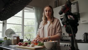 Female cook preparing food and vlogging with her camera mounted on a tripod in kitchen