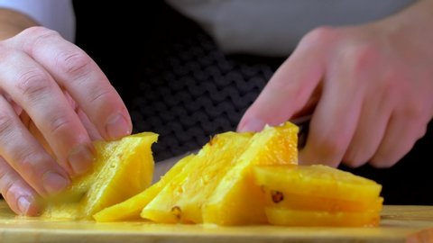 Close up of young man chef hands slicing a pineapple in kitchen macro super male female fruits