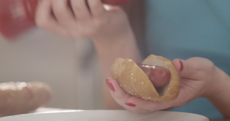 Making Hotdog a Woman Holding a Bun with Sausage and Pouring Ketchup Mustard and Mayo a Closeup shot on Red Camera Royalty-Free Stock Footage #1054539713