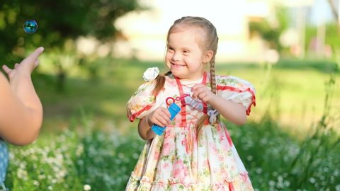 A girl with Down syndrome blows bubbles with mother. The daily life of a child with disabilities. Chromosomal genetic disorder in a child.