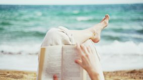 On the beach. A girl lies on the beach and reads a book. Female legs on the sea background. Light breeze. Turquoise waves. Summer chill. Vacation at the sea. Rest and pleasure. Holidays on the beach. - Powered by Shutterstock - Get 15% off with code: PIKWIZARD15