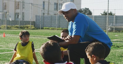 Mixded race male soccer coach instructing a multi-ethnic group of boy soccer players on a playing field in the sun during a soccer training session