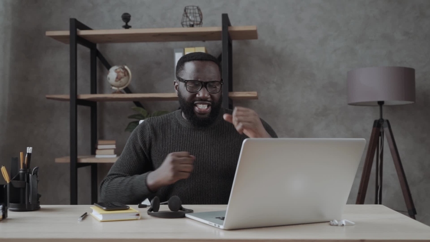 Happy african millennial guy sitting at table look at laptop screen feels excited received great news online lottery winner rejoicing at home, man got promoted or rewarded, hired on dream job concept | Shutterstock HD Video #1054543019