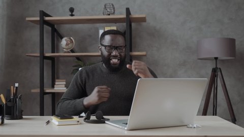 Happy african millennial guy sitting at table look at laptop screen feels excited received great news online lottery winner rejoicing at home, man got promoted or rewarded, hired on dream job concept