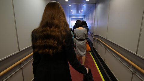 Passengers boarding to plane, people slowly walk, economy class queue at jet bridge. Woman go at end of line with trolley case, first person view camera follow behind