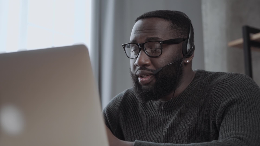African American male, call center agent in headset consult business client online using laptop \ black man in headphones leads an online webinar Royalty-Free Stock Footage #1054549661