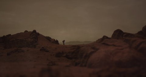 Lonely astronaut walking on a surface of a red rocky planet. Mars colonization concept. Dust effect added